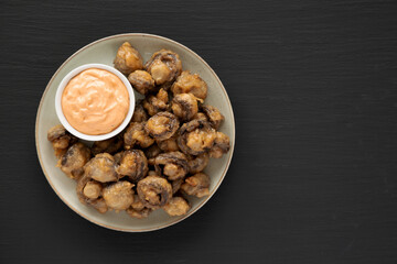 Homemade Crispy Deep Fried Mushrooms with Spicy Mayo on a Plate on a black background, top view. Space for text.