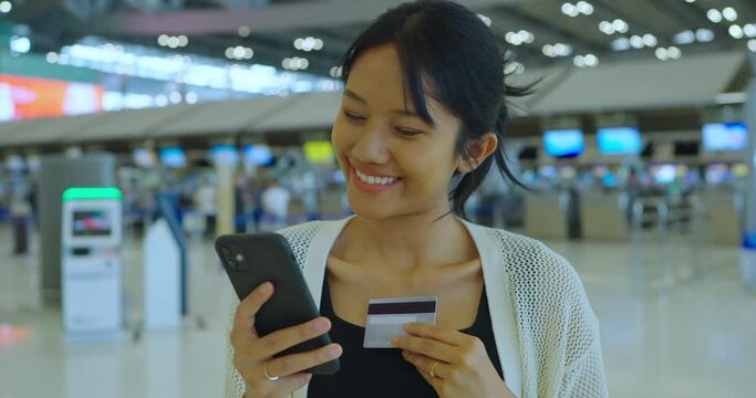 Young asian woman using credit card at airport terminal. She using credit for online booking or shopping with happy expression.