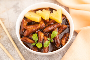 Tteokbokki or Topokki, fried rice cake stick, on gray concrete, side view, selective focus