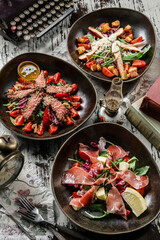 Assorted salads with prosciutto meat, fillet chicken, medium rare beef and vegetables and lettuce in plate on rustic wooden background. Healthy food, close up