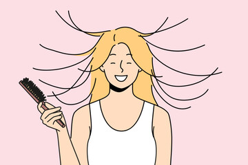Woman combs hair and smiles, seeing effect of static magnetization of hairstyle. Funny young blonde girl takes care of own hair getting ready for date and laughing feeling surge of positive emotions - obrazy, fototapety, plakaty