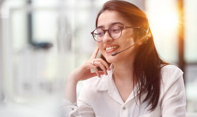 Portrait of a young woman in a headset working in an office center online from a laptop.