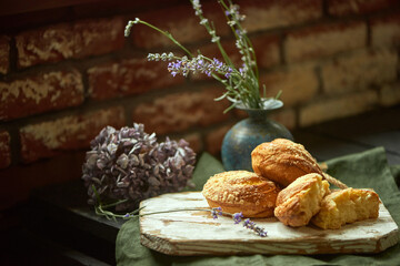 In front of the red brick wall, on a wooden table, there are tasty swirl buns on a light board with a green cloth underneath. Flowers in the background. Concept of country life. Recipe Blog Post