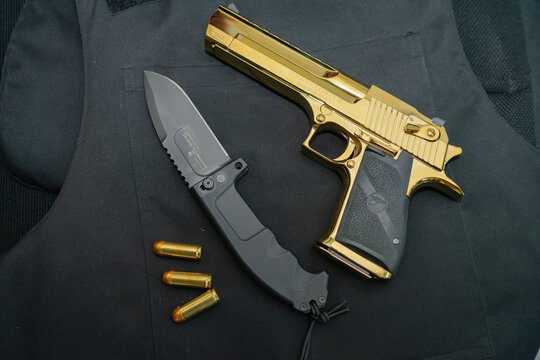 Estonia, Tallinn August 15, 2023.  A powerful Desert eagle 50AE gold-colored pistol and an Italian long-range reconnaissance knife Extrema ratio rao 2.