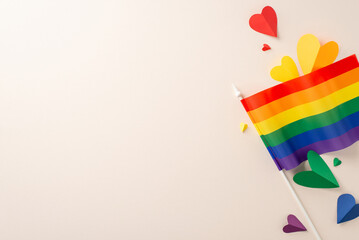Theme of LGBT Month with flat lay top view of pride accessories including rainbow flag and paper hearts against beige background with space for text or message