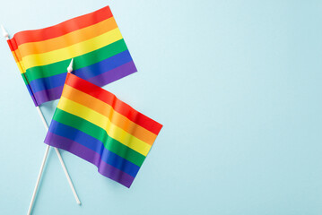 Honoring LGBTQ+ Pride Month in July with colorful pride flags in this captivating top-down view photo, they adorn a calming light blue isolated background, suitable for ads or text incorporation