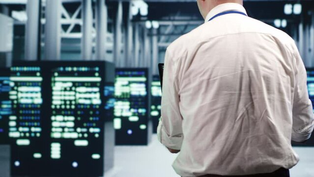 Aged IT consultant in data center, solving tasks on tablet while running scripts on laptop terminal. Trained repairman walking amidst servers, accessing databases and manipulating lines of code