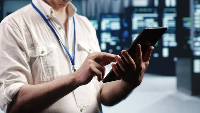 Tech savvy professional navigating network of server rigs in industrial cloud computing company. Manager with tablet doing assessments and optimizations in data center, preventing system pitfalls