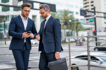 Two business men brainstormed ideas for their next business. Business men analyzed the market trends before making their decision. Two business men using phone outdoor.