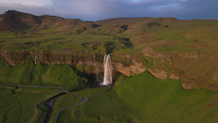 Naklejka premium The Seljalandsfoss waterfall on the south coast of Iceland bathed in the otherworldly light of the midnight sun. The waterfall drops 60 meters and is part of the Seljalands River.