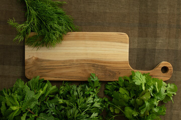 Bunches of fresh herbs, a wooden board on a brown tablecloth. Table top view. Mint, parsley, dill, coriander. Food background. Nutrition, greens, cooking, organic concept. Mock up. Copy space. Nobody