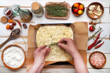 Cooking Homemade Italian flat bread focaccia with cherry tomatoes and chili pepper close up on baking sheet on wooden table. View from above.
