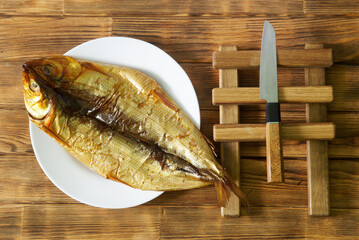 Prepared gutted smoked Baikal omul in a white plate on a wooden table made of pine boards next to a knife. Rare fish delicacy - omul. Photo