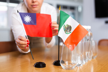 Unrecognizable woman preparing room for international negotiations and communication discussions of leaders. Lady sets miniatures flags of Mexico and Taiwan on table. Unfocused shot