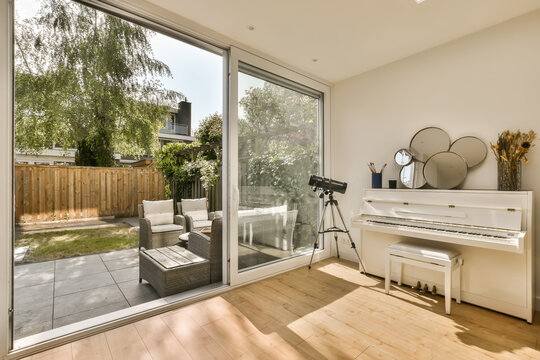 a living room with a piano in the center and an open patio door leading to the back yard on the right side