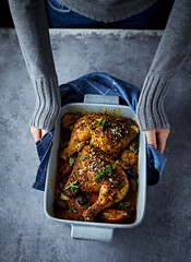 Woman hands holding a ceramik dish with oven-baked chicken legs. Top view. Home cooking concept - 638657865