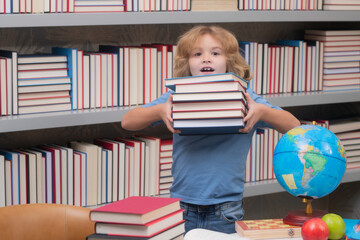 School boy with stack of books in library. Back to school. Funny little child from elementary school with book. Education. Kid study and learning.