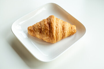 Croissant bread in a white plate lies on a white table