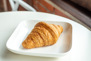 Croissant bread in a white plate lies on a white table