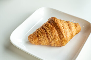 Croissant bread in a white plate lies on a white table