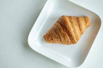 Croissant bread in a white plate lies on a white table