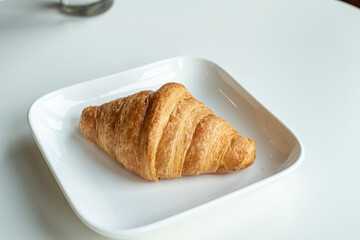 Croissant bread in a white plate lies on a white table