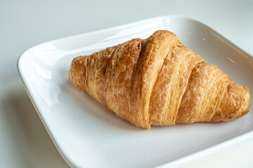 Croissant bread in a white plate lies on a white table