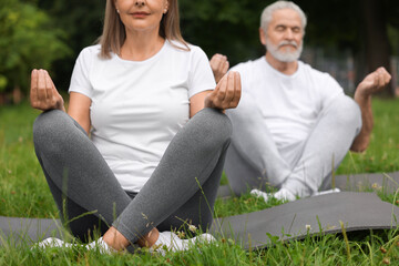 Senior couple practicing yoga on green grass in park, selective focus