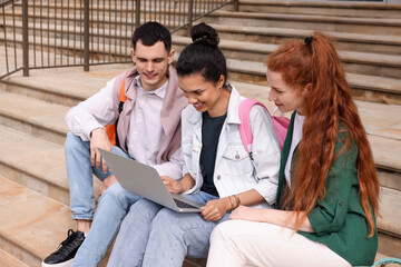 Happy young students studying together with laptop on steps outdoors