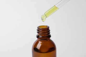Dripping cosmetic oil from pipette into bottle on white background, closeup