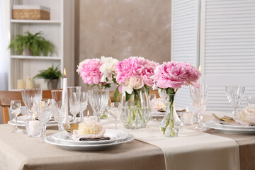 Stylish table setting with beautiful peonies and burning candles indoors