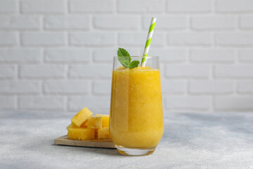 Glass of tasty pineapple smoothie and cut fruit on light gray table