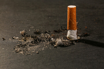 Burnt cigarette and ash on black table, closeup. No smoking concept