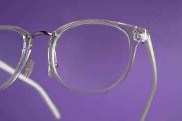 Stylish pair of glasses on purple background, closeup