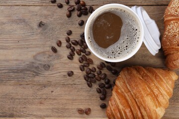 Coffee to go. Paper cup of tasty drink, croissants and beans on wooden table, flat lay with space for text