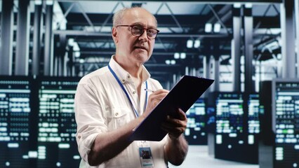 Elderly engineer looking around high tech data center, using clipboard to crosscheck disaster recovery plan and assess server components in need of replacement, preventing failures