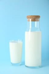 Carafe and glass of fresh milk on light blue background