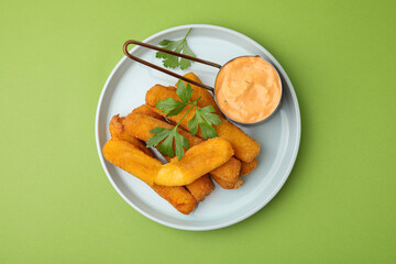Tasty fried mozzarella sticks served with sauce and parsley on green background, top view