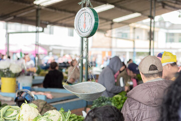 A day at the local market. Unrecognizable people shopping at a farmer's market. Hanging scale....