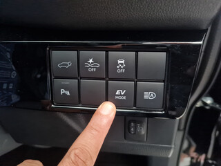 The driver's hand presses the electric vehicle mode (EV MODE) button, which is used in hybrid cars (HV) and plug-in hybrid cars (PHEV).  modern features in hybrid cars for economical and environmental