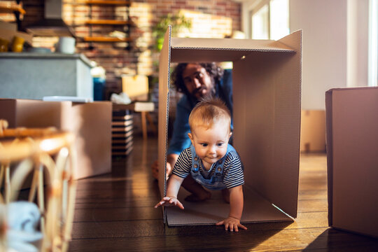 Young father and baby daughter playing with a cardboard box after moving in their new home apartment