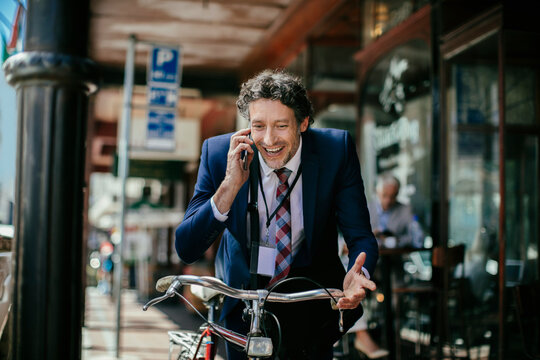 Young caucasian businessman talking on his smart phone and hearing good news while commuting to work with his bicycle