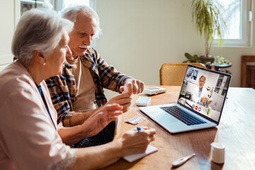 Concerned and worried senior caucasian couple talking to their doctor over a video call on their laptop in the kitchen