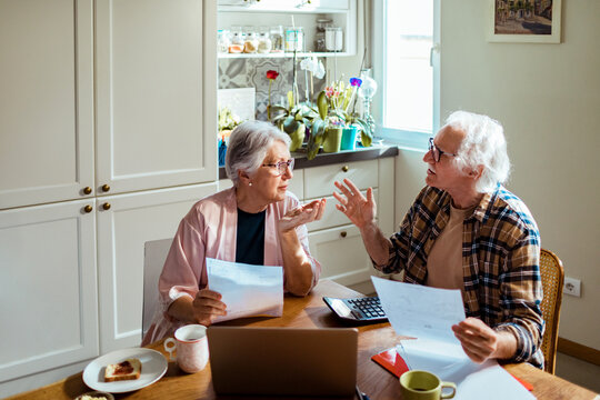 Senior couple having breakfast and arguing while going over their home finances and bills in the kitchen in the morning