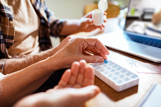 Concerned And Worried Senior Caucasian Couple Talking To Their Doctor Over A Video Call On Their Laptop In The Kitchen And Taking Perscription Medicine