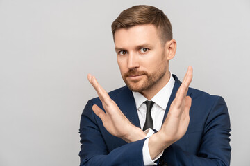 Serious businessman showing a stop sign of failure. Disagreeing indignant man in suit making disapproval gesture with hands, dislike, stop sign, looking at camera, isolated on gray studio background