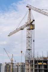 Fototapeta na wymiar A crane and a building under construction against a blue sky background. Builders work on large construction sites, and there are many cranes working in the field of new construction.