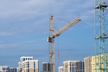 A crane and a building under construction against a blue sky background. Builders work on large construction sites, and there are many cranes working in the field of new construction.