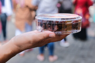 Hand showing a plastic container filled with crispy fried grasshoppers