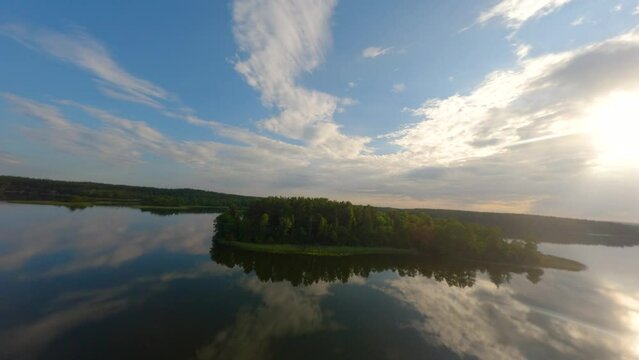 Drone approaching and island in lake Baluosas in Lithuania with calm water reflecting clouds lika a mirror